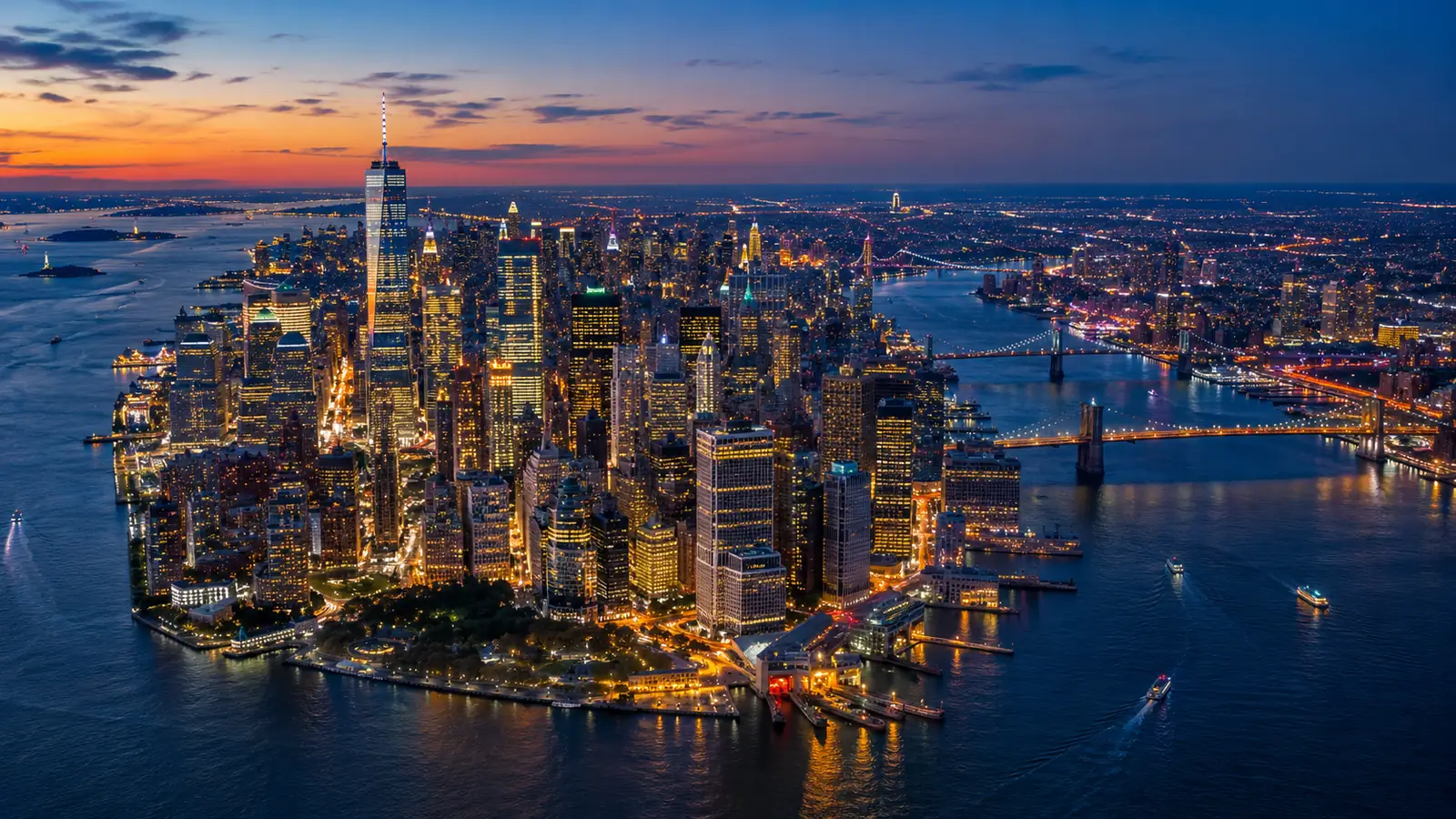 Lower Manhattan lit up at dusk from the air, the East River bridges glowing on the right
