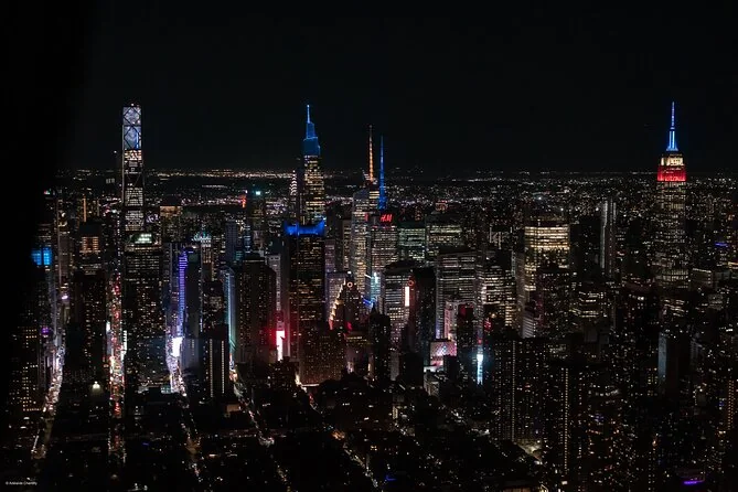 Midtown Manhattan's towers lit up at night, the Empire State Building glowing red, white and blue