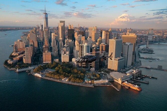 A tour helicopter flying past Lower Manhattan in evening light, Battery Park below
