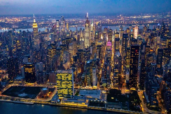 Midtown Manhattan at night from the air, the United Nations headquarters on the East River in front and the Empire State Building on the left